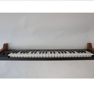 K&ouml;nnte beinhalten: Ein Wandregal aus Holz mit einer schwarzen Tastatur darauf. Das Regal ist aus dunkelbraunem Holz und hat ein schlichtes Design.