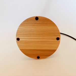 May include: A round wooden base with four black rubber feet. The base is made of light wood with a natural grain pattern.