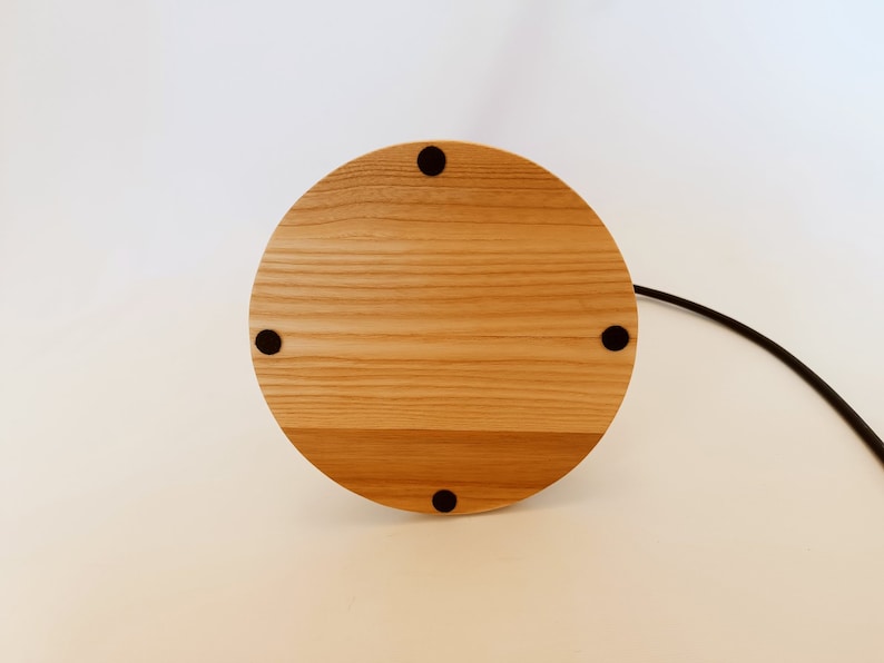 May include: A round wooden base with four black rubber feet. The base is made of light wood with a natural grain pattern.