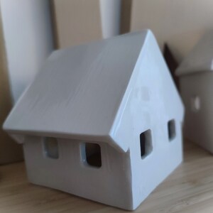 May include: Two white ceramic houses with cut-out windows. The houses are sitting on a wooden surface.