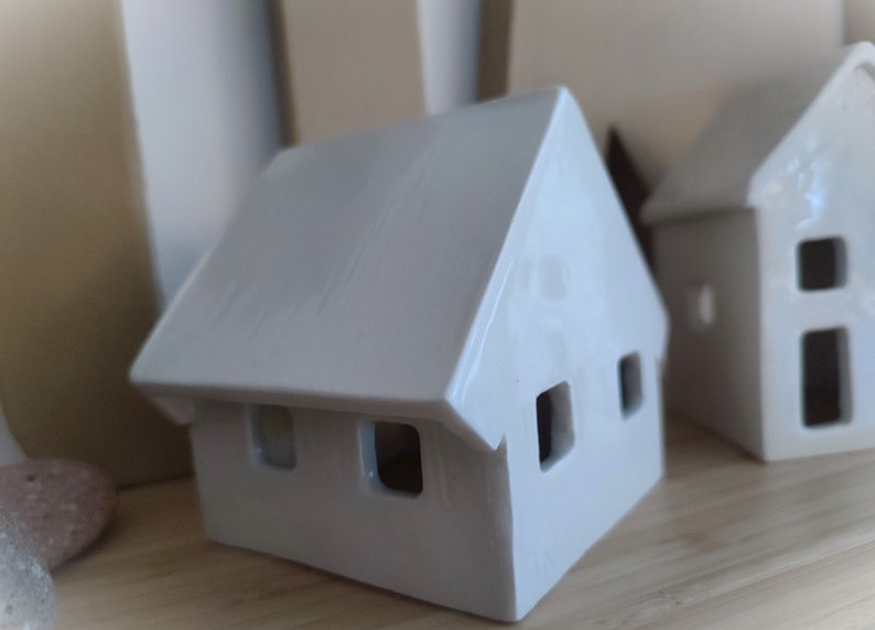 May include: Two white ceramic houses with cut-out windows. The houses are sitting on a wooden surface.