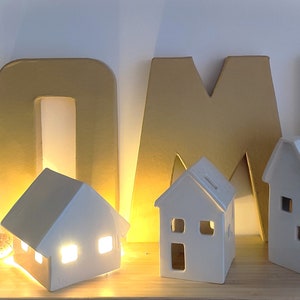 May include: White ceramic houses with lit windows, arranged in front of gold cardboard letters spelling "HOME".