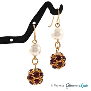 May include: Gold dangle earrings with a white pearl and a burgundy crystal ball.