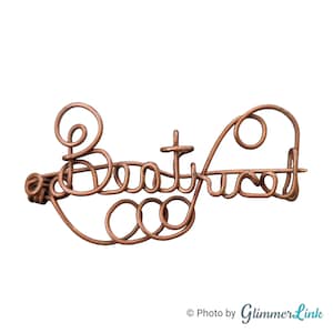May include: A copper-toned wire sculpture spelling "Beautyfied" in cursive. The word is formed from looped and swirled wire, creating a decorative, artistic piece. The background is white.