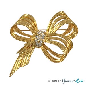 May include: A gold-toned bow brooch with a large rhinestone centre. The bow is made of multiple layers of metal and has a textured finish.