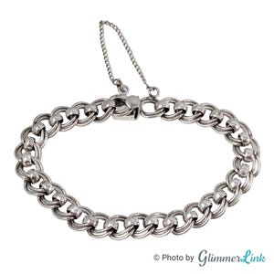 May include: A silver-toned metal chain link bracelet featuring a series of interlocking circular links. The bracelet includes a secure box clasp mechanism and a thin safety chain attached to the clasp to prevent accidental loss during wear.
