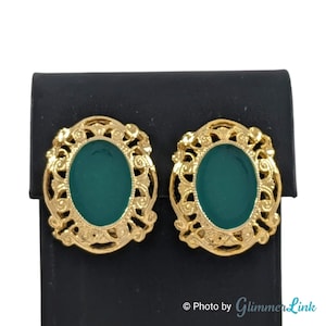 May include: A pair of gold tone clip-on earrings with green oval-shaped stones set in a filigree design.