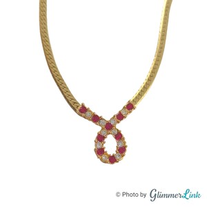 May include: A gold chain necklace with a pendant featuring a circle of red and white rhinestones.