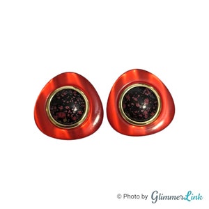 May include: A pair of red, triangular-shaped earrings with a gold rim and a black and pink speckled center.