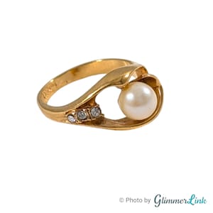 May include: A gold ring with a pearl and small clear stones. The ring is designed with a curved band that holds the pearl in a small open space.