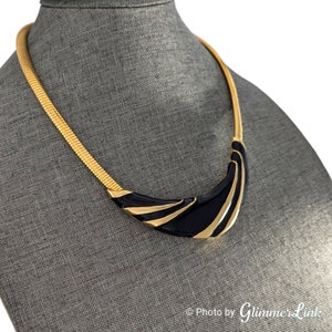 May include: A gold tone choker necklace with a black enamel pendant. The pendant is shaped like a crescent moon with gold accents.