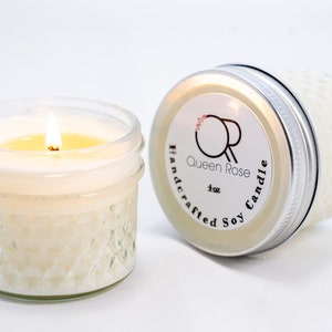 May include: A 4 oz soy candle in a clear glass jar with a silver lid. The candle is lit and the flame is visible. The jar has a textured design. The lid has a label that says "Queen Rose Handcrafted Soy Candle".