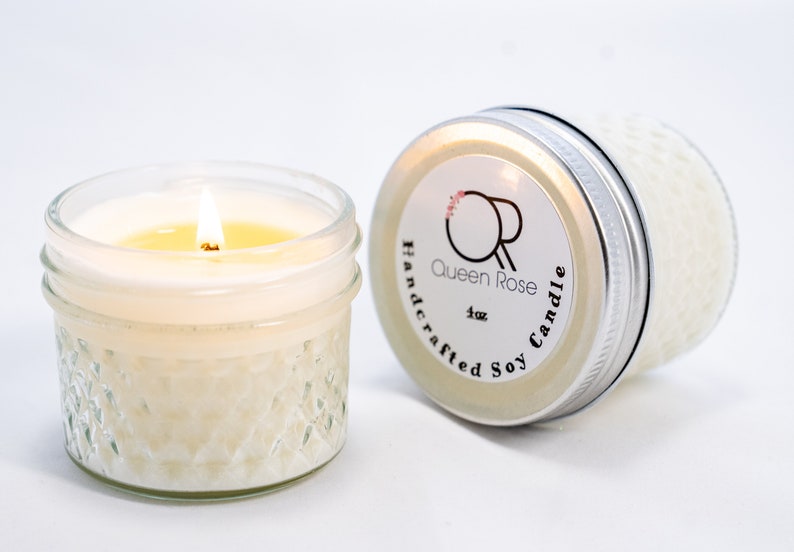 May include: A 4 oz soy candle in a clear glass jar with a silver lid. The candle is lit and the flame is visible. The jar has a textured design. The lid has a label that says "Queen Rose Handcrafted Soy Candle".