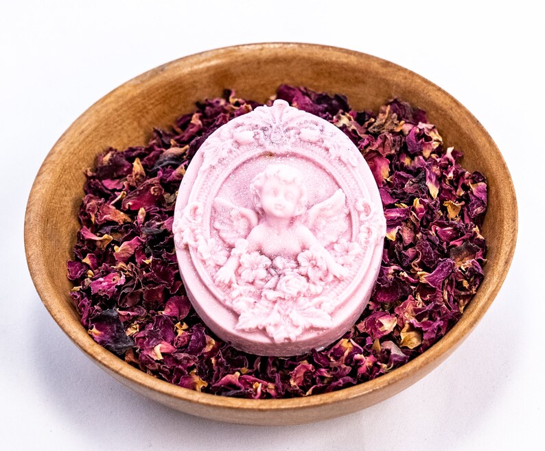 May include: A pink oval-shaped soap with a cherub design in a wooden bowl filled with dried rose petals.