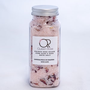 May include: A clear glass jar with a silver lid filled with pink bath salts and dried rose petals. The label reads "Queen Rose French Rose Relax Pink Clay & Rose Bath Salt Handblended in Virginia with Love."