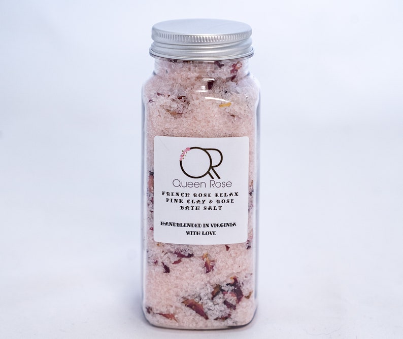 May include: A clear glass jar with a silver lid filled with pink bath salts and dried rose petals. The label reads "Queen Rose French Rose Relax Pink Clay & Rose Bath Salt Handblended in Virginia with Love."