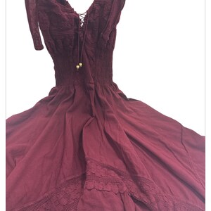 Puede incluir: Un vestido maxi sin mangas de color burdeos con un borde de encaje y un detalle de cord&oacute;n en el escote.