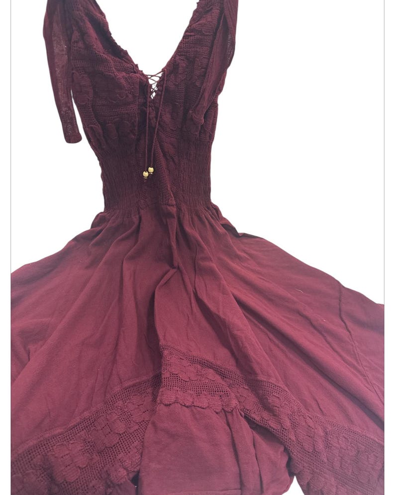 Puede incluir: Un vestido maxi sin mangas de color burdeos con un borde de encaje y un detalle de cord&oacute;n en el escote.