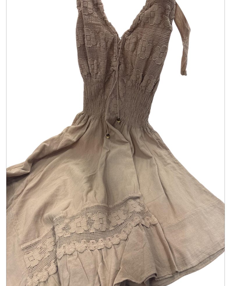 Puede incluir: Un vestido sin mangas de color marr&oacute;n claro con un corpi&ntilde;o de encaje y un borde de encaje en el dobladillo. El vestido tiene un corpi&ntilde;o ajustado y una falda fluida.