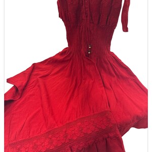 Puede incluir: Un vestido rojo de crochet con un corpi&ntilde;o ajustado y una falda fluida. El vestido tiene un borde de encaje en la parte inferior y un lazo en el escote.