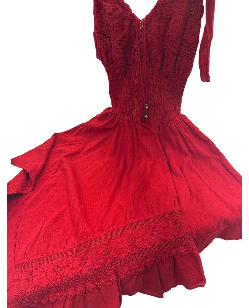 Puede incluir: Un vestido rojo de crochet con un corpi&ntilde;o ajustado y una falda fluida. El vestido tiene un borde de encaje en la parte inferior y un lazo en el escote.