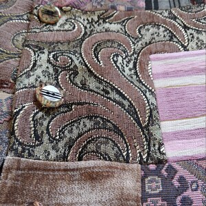 K&ouml;nnte beinhalten: Nahaufnahme eines Patchwork-Stoffs mit verschiedenen Mustern und Texturen. Das Design umfasst Paisley-, Blumen- und Streifenelemente in Braun-, Gold- und Rosat&ouml;nen. Dekorative Kn&ouml;pfe sind sichtbar.