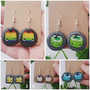 May include: A set of six pairs of handmade earrings featuring pixelated designs. The earrings are made of polymer clay and have silver hooks. The designs include a rainbow, a green block, a yellow block, a pink block, and two blue blocks.