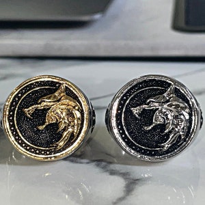 May include: Two round rings with a wolf head design. One ring is gold-colored with a black background, and the other is silver-colored with a black background. Both rings have a detailed wolf head in the center.