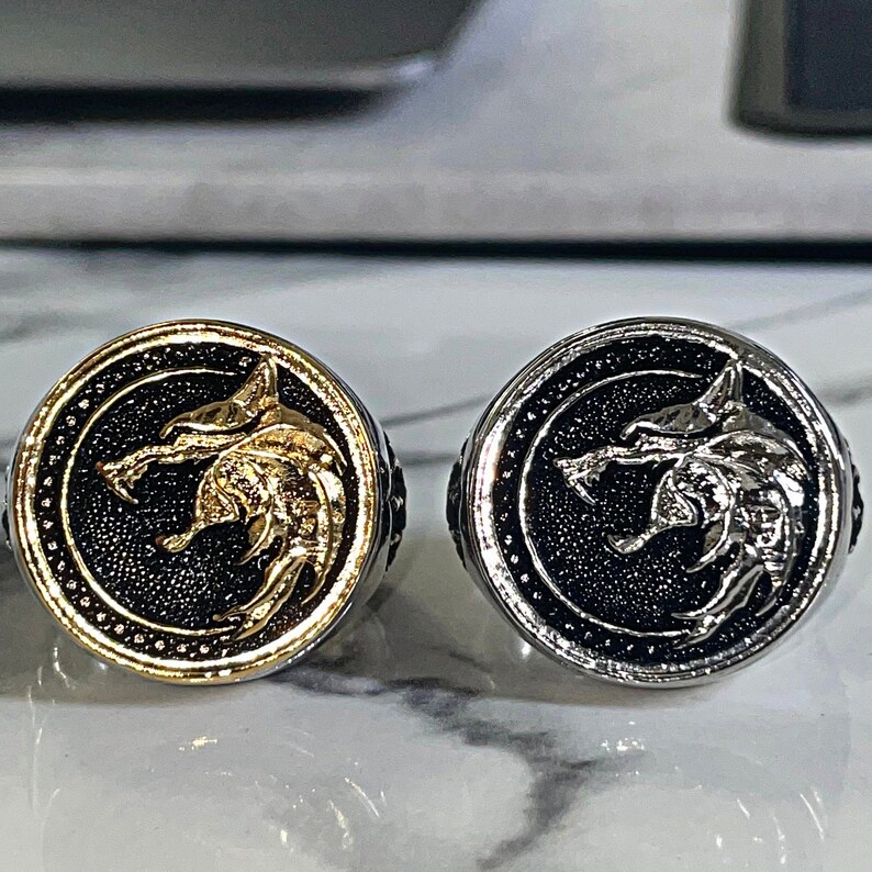 May include: Two round rings with a wolf head design. One ring is gold-colored with a black background, and the other is silver-colored with a black background. Both rings have a detailed wolf head in the center.