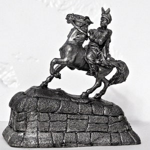 May include: A pewter figurine of a man on horseback, the horse is rearing up on its hind legs, the man is wearing a feathered hat and a long coat, the figurine is on a stone base.