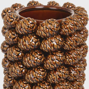 May include: A cylindrical ceramic vase featuring a textured exterior covered in a repeating pattern of glossy brown pinecones. The vessel has a smooth, dark brown interior rim and a hollow centre, showcasing a uniform, glazed finish throughout.