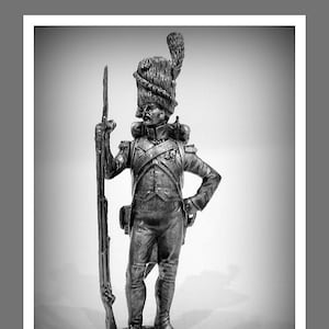 May include: A black and white figurine of a soldier wearing a tall, feathered hat and holding a rifle. The soldier is standing on a base.