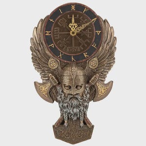 May include: A bronze-colored wall clock with a Viking theme. The clock face has Roman numerals and a compass design. The clock is adorned with a Viking helmet, axes, wings, and a long beard. The clock measures approximately 12 inches in height.