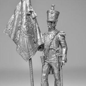 May include: A monochrome figurine of a soldier holding a flag. The soldier is in uniform, with a tall hat and sword. The flag is detailed, with tassels and a decorative top. The figurine is on a small, round base.