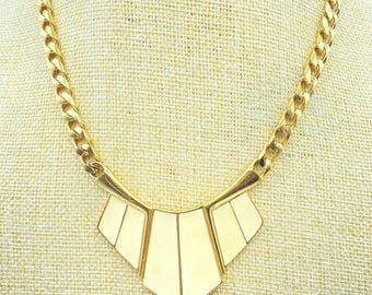 May include: A gold-tone chain necklace featuring a central geometric pendant. The pendant consists of three cream-colored, fan-shaped panels framed in gold metal, suspended from a thick, interlocking curb chain with a polished metallic finish.