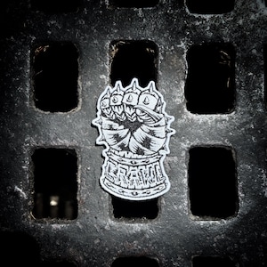 May include: A black and white embroidered patch featuring a stylized armored gauntlet fist with spiked knuckles. The word CRAWL is stitched in a bold, blocky font across the wrist cuff section of the gauntlet design, which has a thick white border.