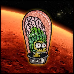 May include: Embroidered patch of a green and pink alien head in a glass dome, against a red and orange background resembling Mars.