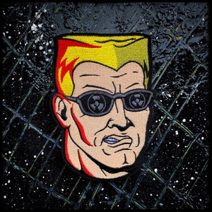 May include: A cartoon illustration of a man with a yellow and red mohawk hairstyle wearing black sunglasses with a nuclear symbol on each lens. The man has a serious expression on his face.
