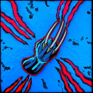 May include: An embroidered patch featuring a blue hand with three long, sharp silver claws extending from the knuckles. The design is outlined in red and set against a bright blue background with red claw mark slashes in the corners.