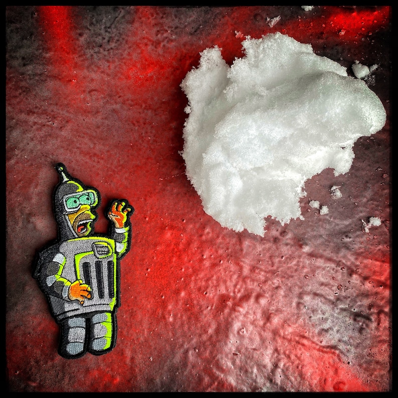 May include: A robot with a yellow face and green eyes is standing on a red and black background. The robot is wearing a silver suit and has a yellow antenna on its head. The robot is looking up at a large white cloud.