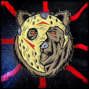 May include: A brown bear wearing a yellow and red hockey mask. The mask has a black strap and a black eye hole on each side. The bear's fur is brown and the mask is covering the top half of the bear's face.