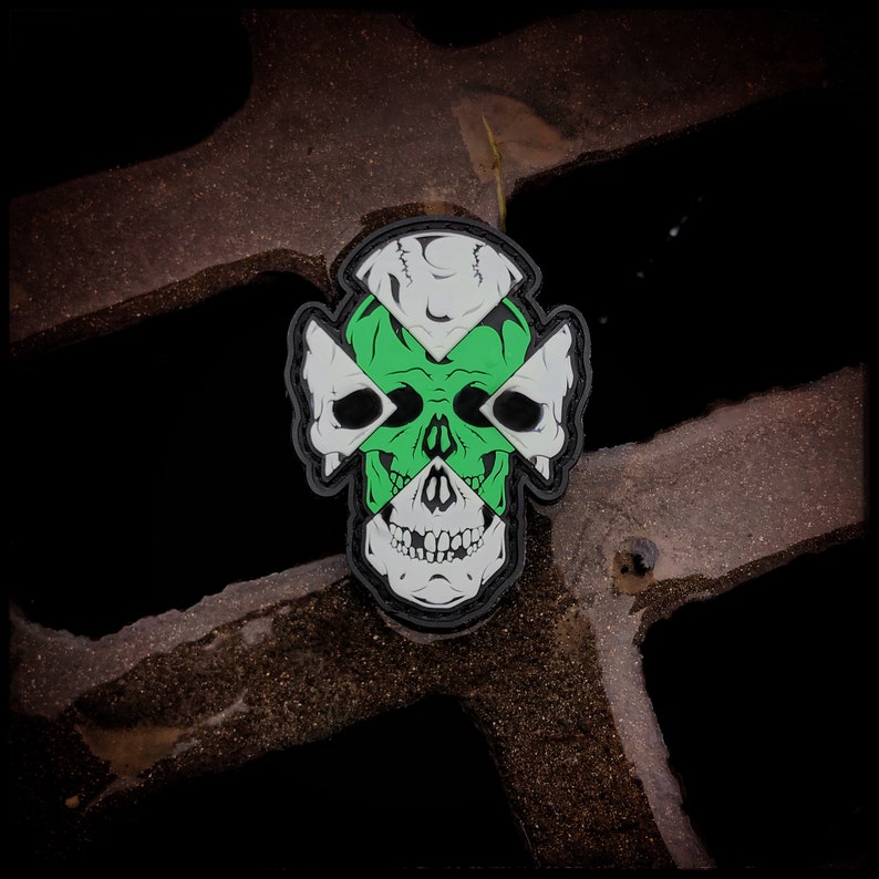 May include: A green, white, and black skull patch with a cross design. The skull is stylized with a cross pattern over the eyes and nose.