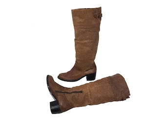 May include: A pair of brown knee-high boots. One boot stands upright, while the other lies on its side. Both boots have a textured appearance, a small heel, and a buckle detail near the top.