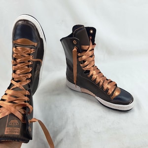 May include: High-top sneakers in dark brown and navy blue with copper-colored satin laces. The sneakers have a white sole and a metallic copper accent on the toe and heel. The Adidas logo is visible on the side.