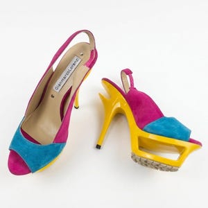 May include: A pair of Gianmarco Lorenzi slingback high heels featuring a vibrant color-blocked design in magenta, bright blue, and yellow. The shoes have an open-toe front, a high stiletto heel, and a platform sole with a cutout architectural detail.