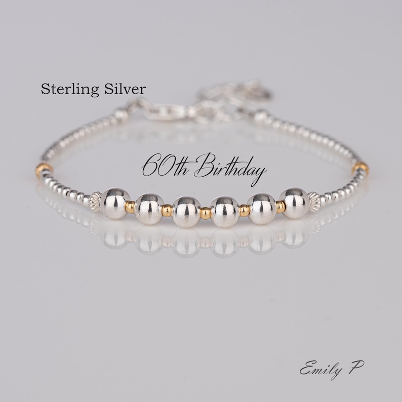 K&ouml;nnte beinhalten: Sterling-Silber-Armband mit abwechselnden silbernen und goldenen Perlen. Das Armband tr&auml;gt den Text "60th Birthday".