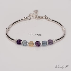May include: A silver bracelet featuring a row of fluorite beads in shades of purple, blue, and yellow. The bracelet has a simple, elegant design and is ideal for everyday wear.