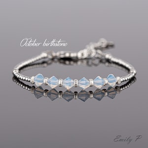 May include: A silver bracelet with a row of light blue opal beads. The bracelet is on a grey background and the text "October birthstone" is above the bracelet.