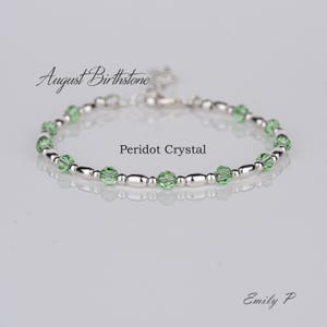 Peut inclure: Un bracelet en argent avec des cristaux de péridot verts et le texte "August Birthstone" et "Peridot Crystal". Le bracelet est sur un fond blanc.