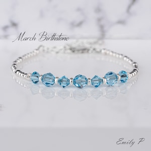 Könnte beinhalten: Ein silbernes Armband mit einer Reihe hellblauer Kristallperlen. Das Armband ist mit "März-Geburtsstein" beschriftet.